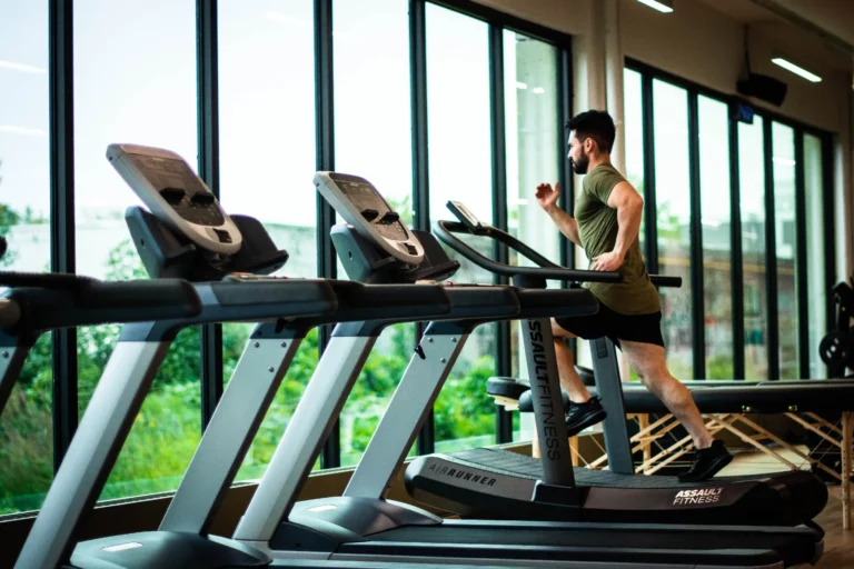 Man in sportschool aan het hardlopen op een hardloopband om te werken aan zijn conditie.